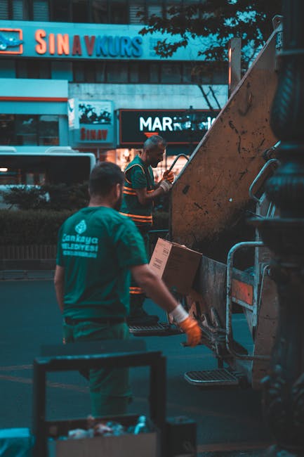 A street scene in Eastcote featuring a waste collection truck operated by Man with Van Eastcote. The truck, parked alongside a narrow cobblestone road, has its rear open, revealing an empty waste comp